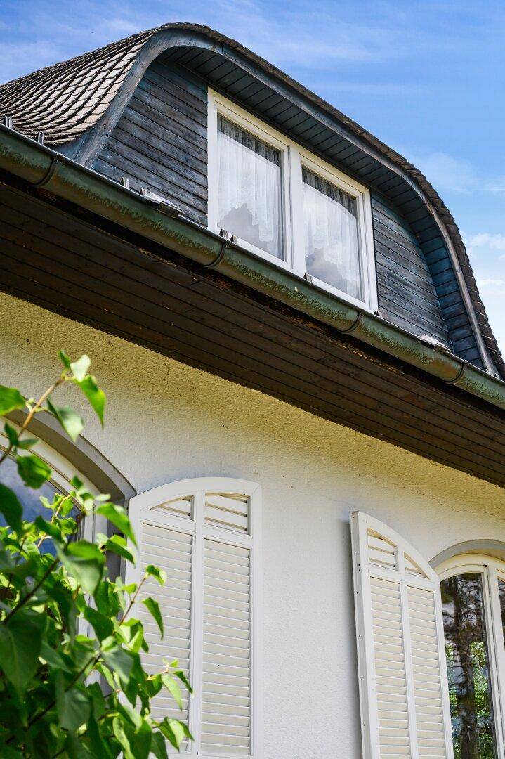 Detailansicht des geschwungenen Mansarddachs und der Fenster mit weißen Fensterläden.