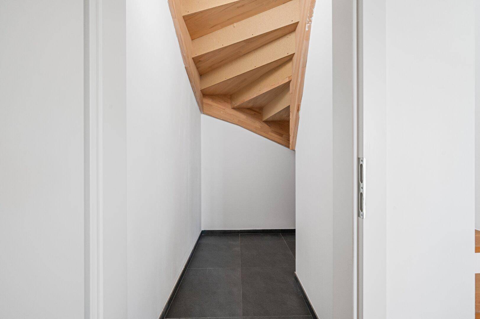 Bereich unter der Treppe mit dunklem Fliesenboden, ideal als zusätzlicher Stauraum.