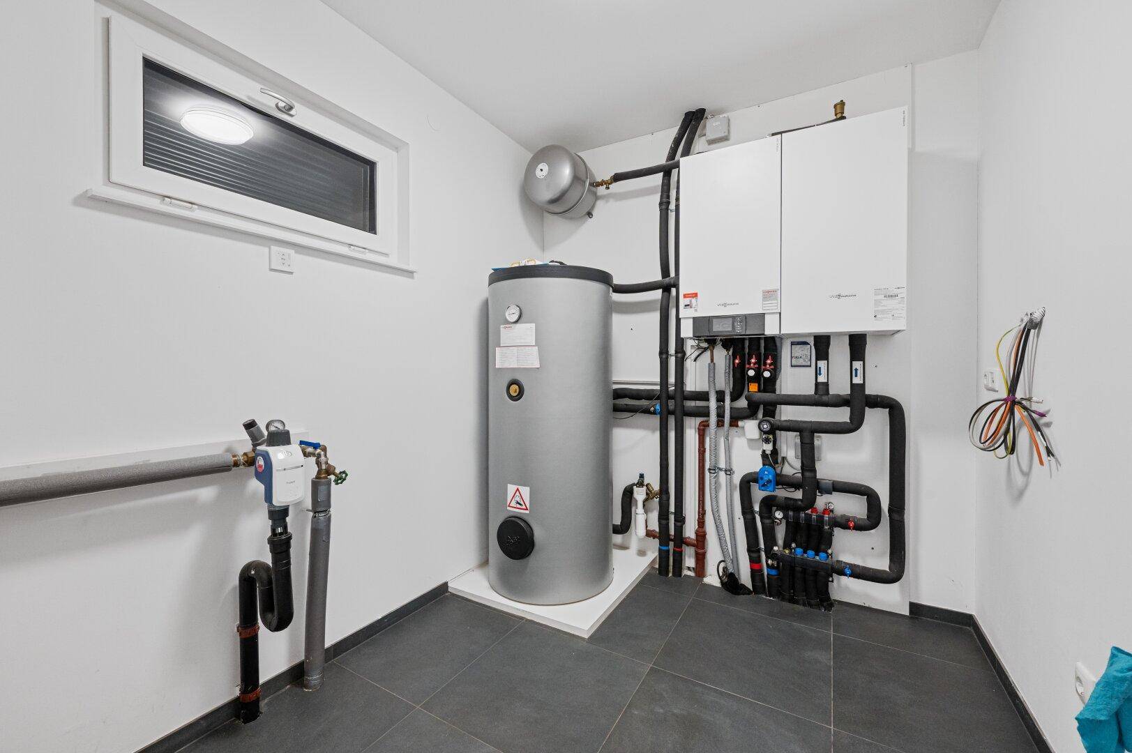 Technikraum mit moderner Heizungsanlage, Warmwasserspeicher und Fenster.