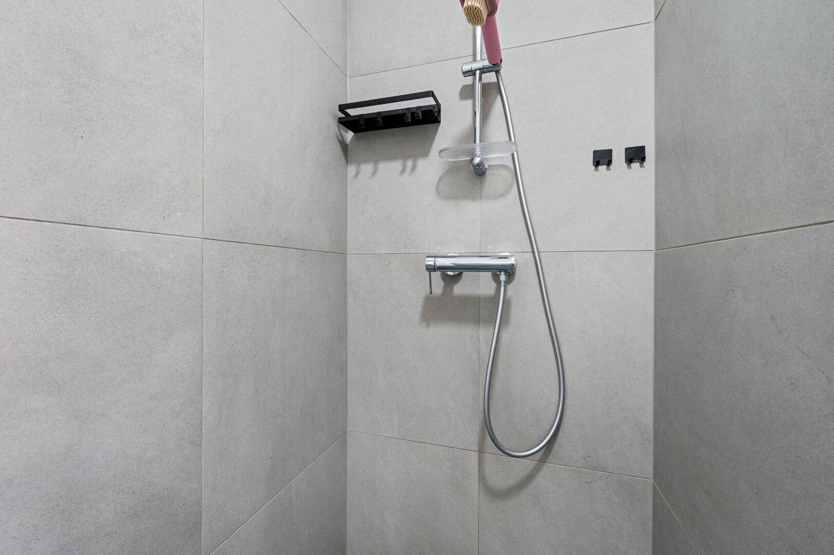 Modern geflieste Dusche mit Handbrause und Ablagefläche in hellem Grau.