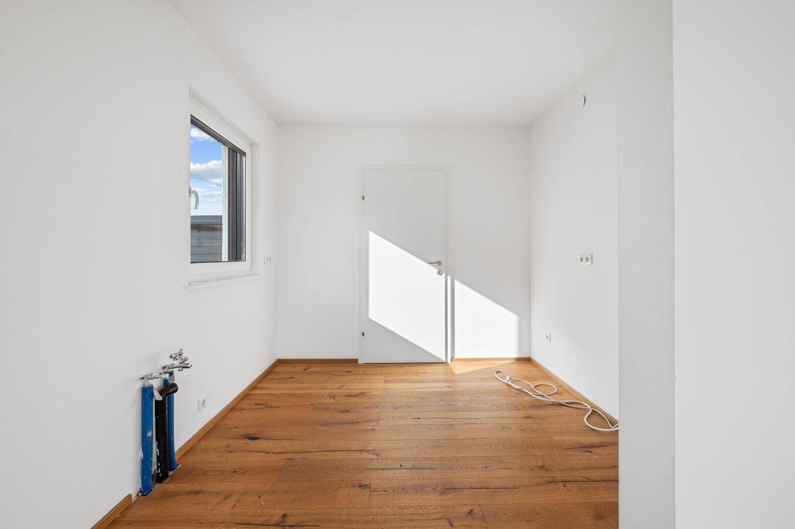 Leerer Raum mit Holzboden und Anschlüssen, ideal für eine Waschküche oder kleine Küche.