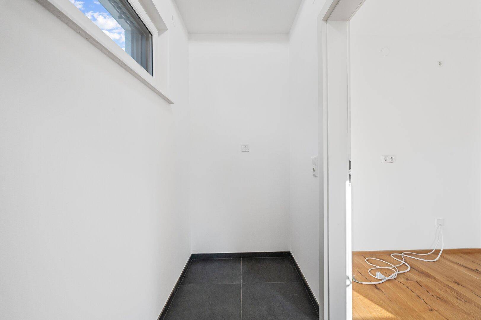 Praktischer Abstellraum unter der Treppe mit dunklen Fliesen und kleinem Fenster.