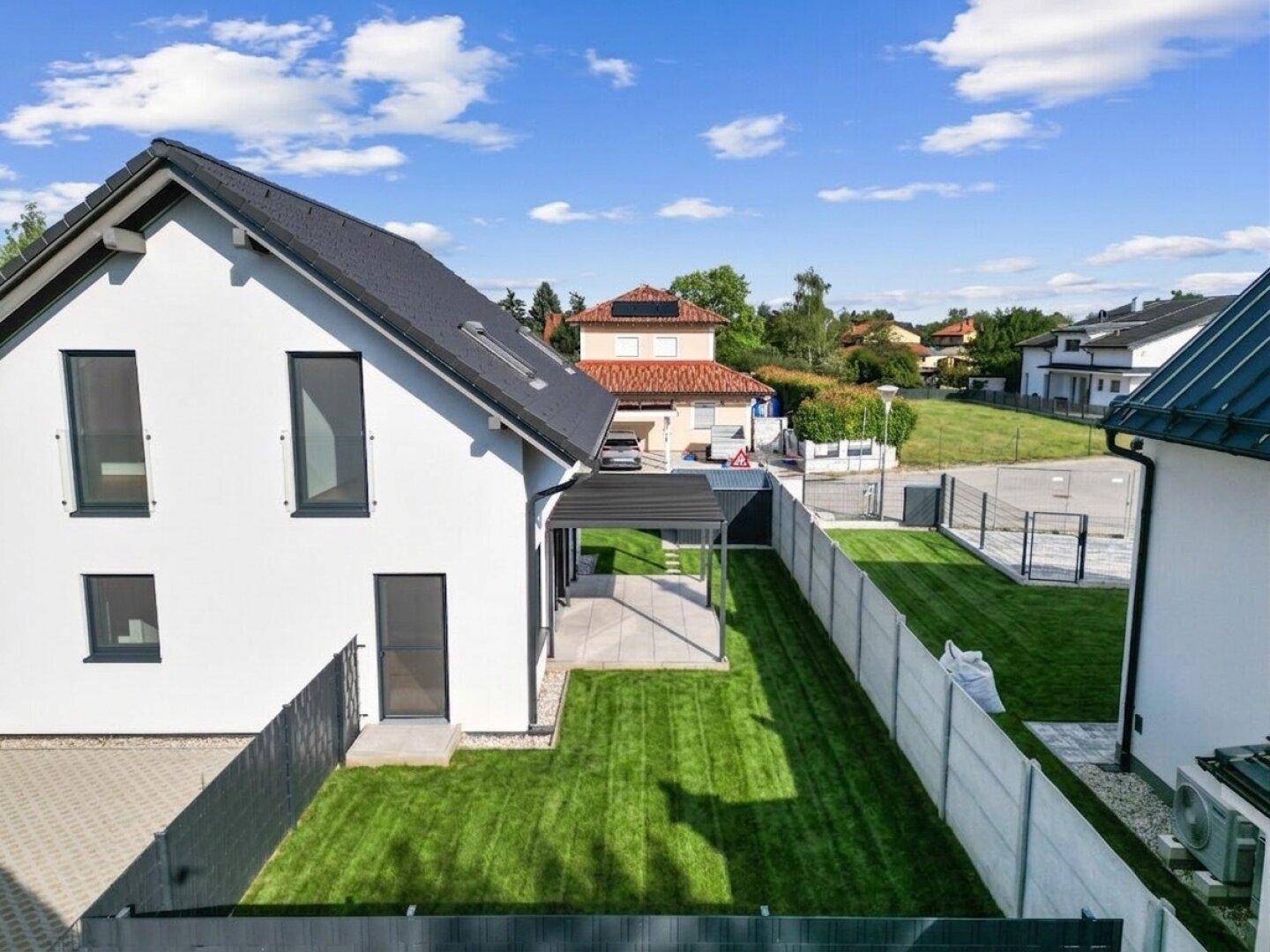 Luftaufnahme eines modernen Einfamilienhauses mit gepflegtem Rasen und Carport.