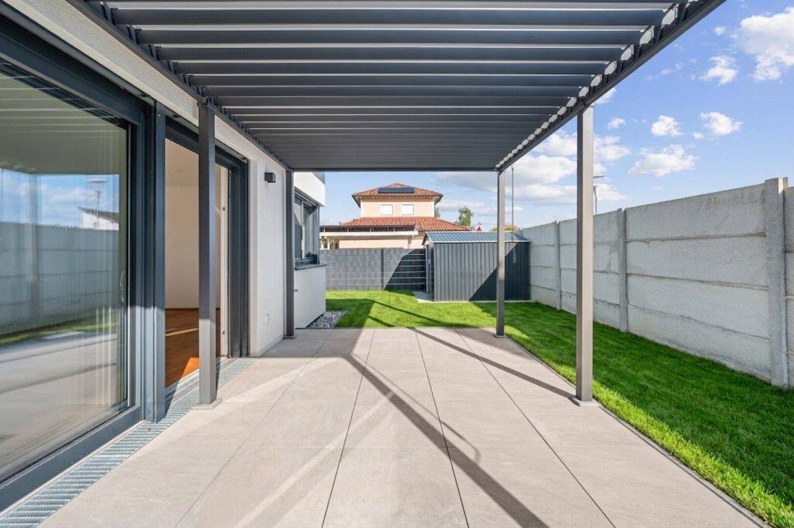 Geräumige, geflieste Terrasse mit moderner Pergola und Zugang zum Garten.