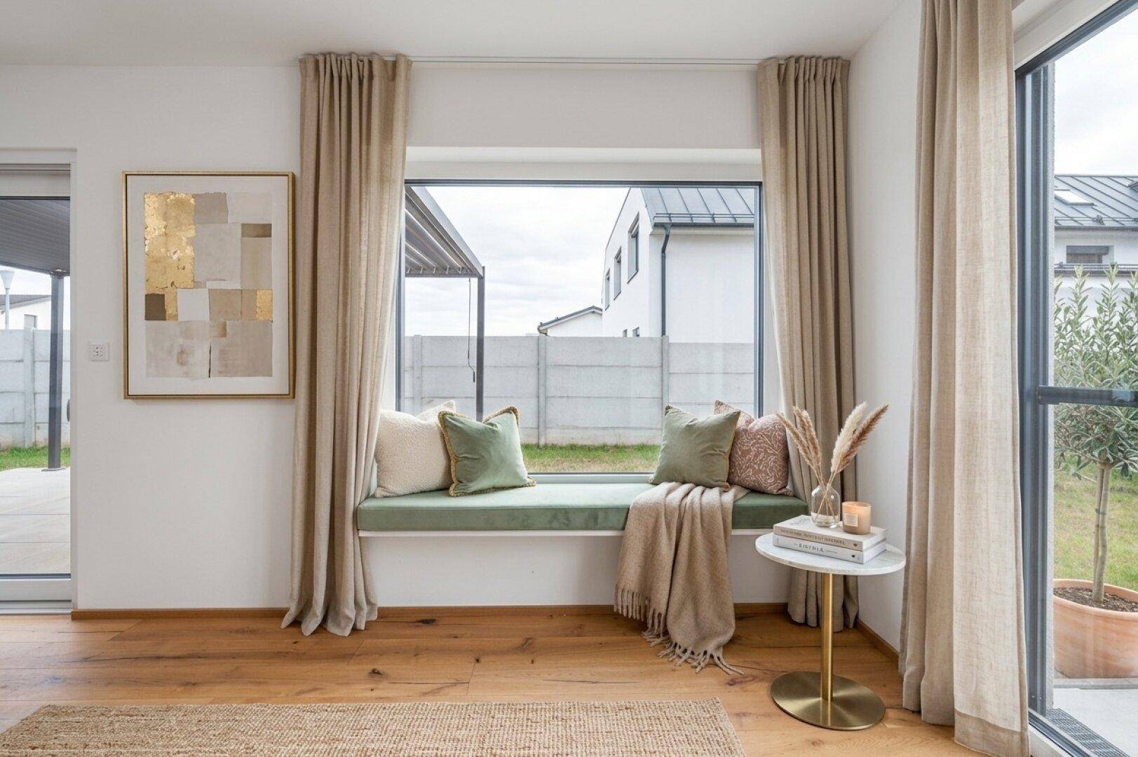 Gemütliche Fenstersitzbank mit Kissen und Blick auf den Garten, ergänzt durch helle Vorhänge.