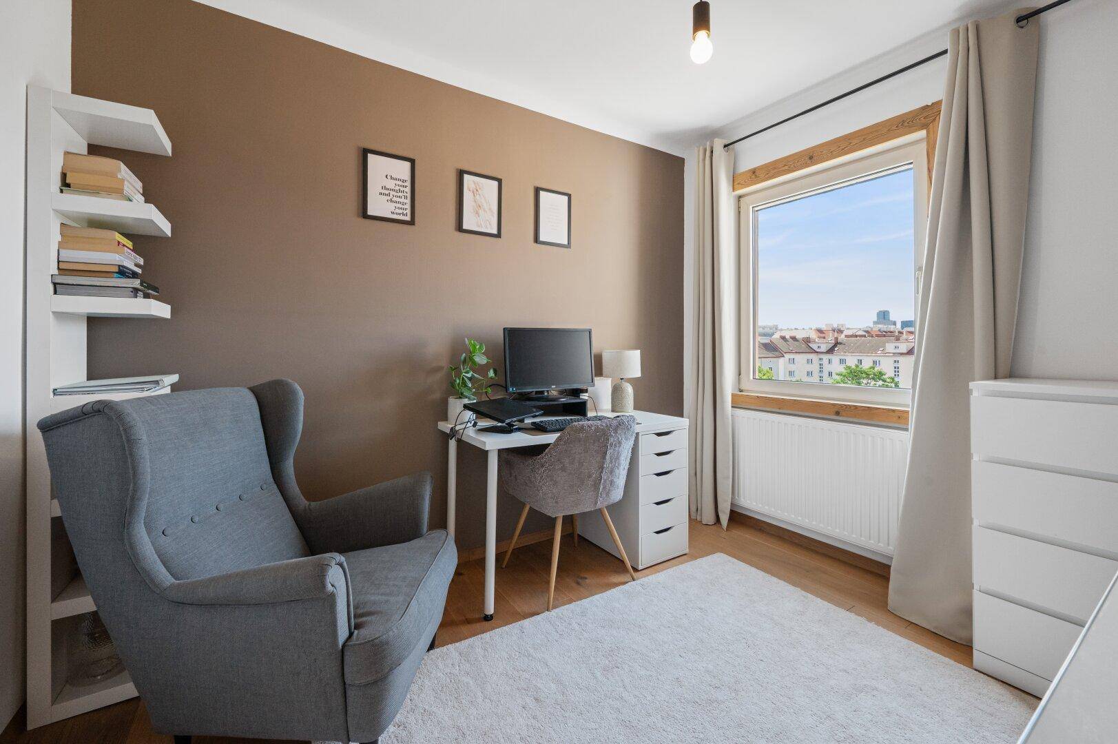 Funktionales Arbeitszimmer mit Schreibtisch, Sessel und Bücherregal, gut beleuchtet durch das Fenster.