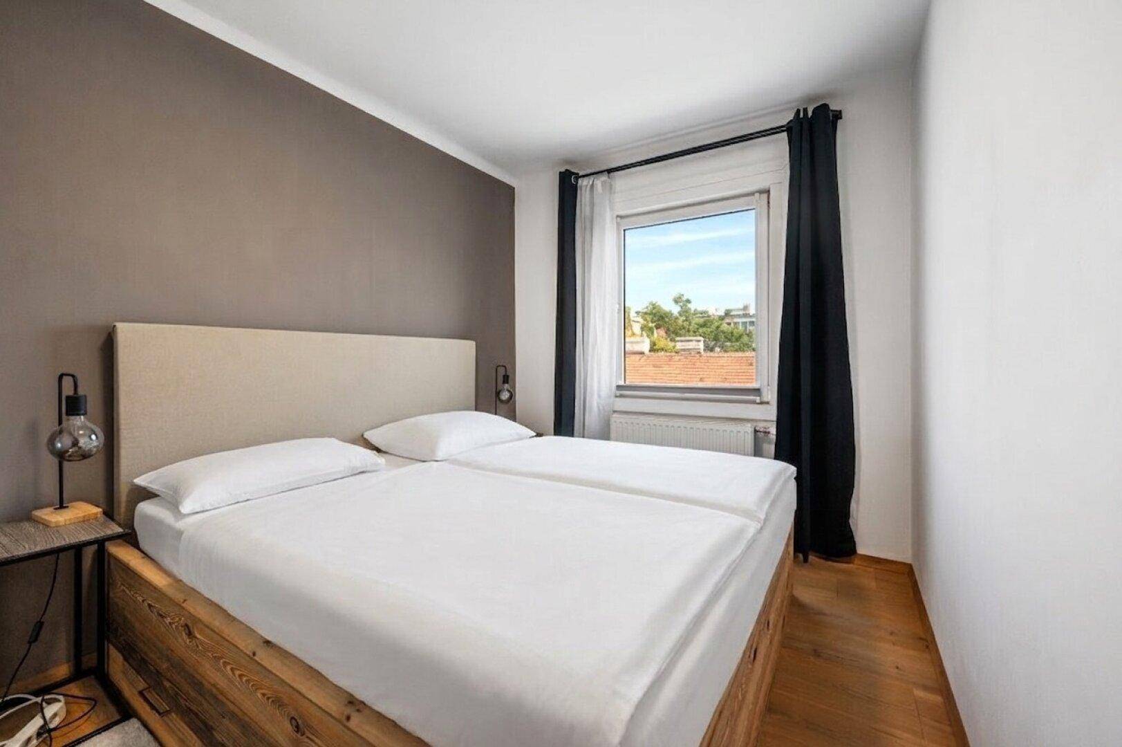 Helles Schlafzimmer mit Doppelbett, Holzboden und Fenster mit Blick auf die Umgebung.