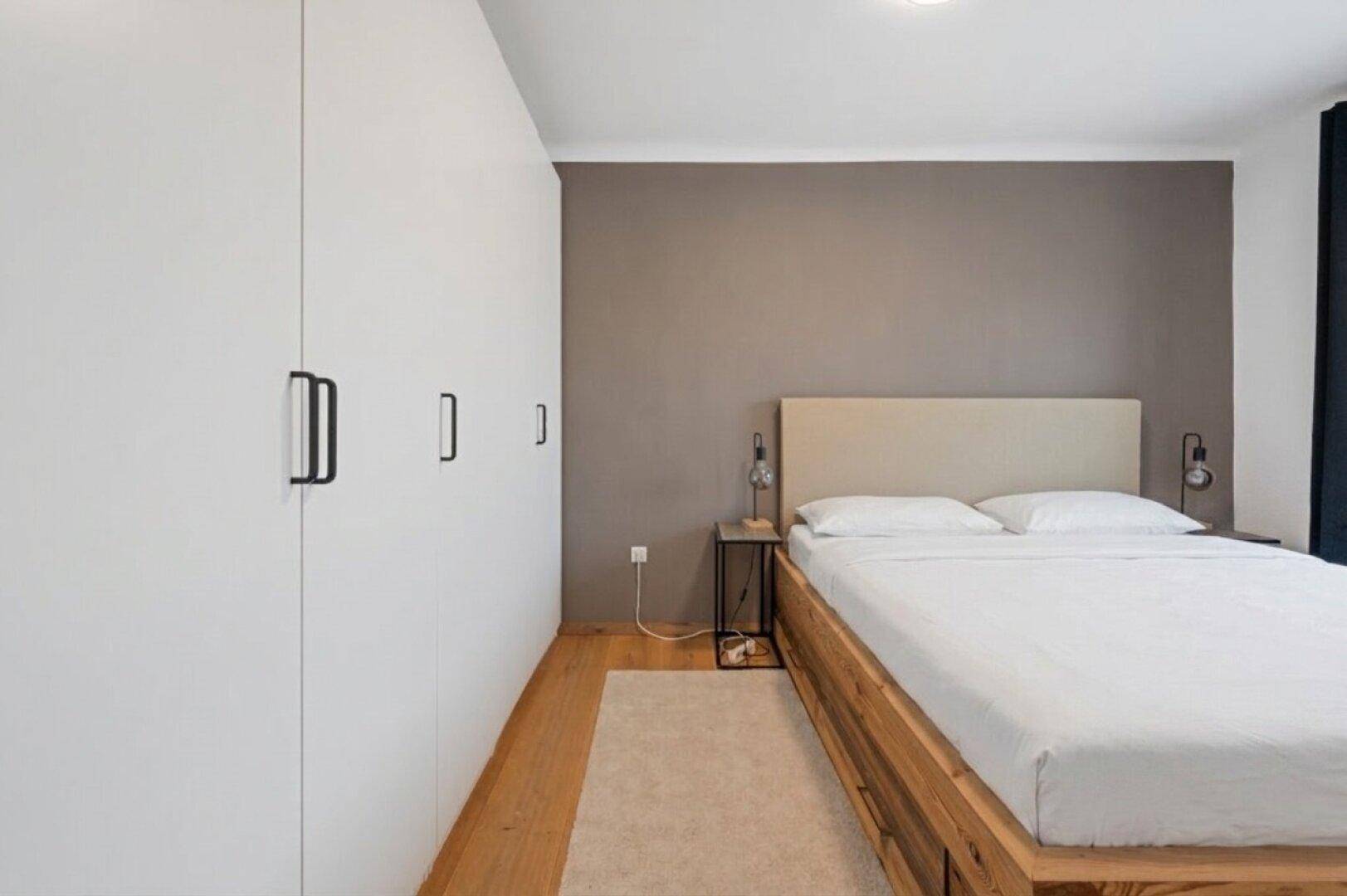 Schlafzimmer mit Doppelbett, Holzboden und großen weißen Einbauschränken für viel Stauraum.