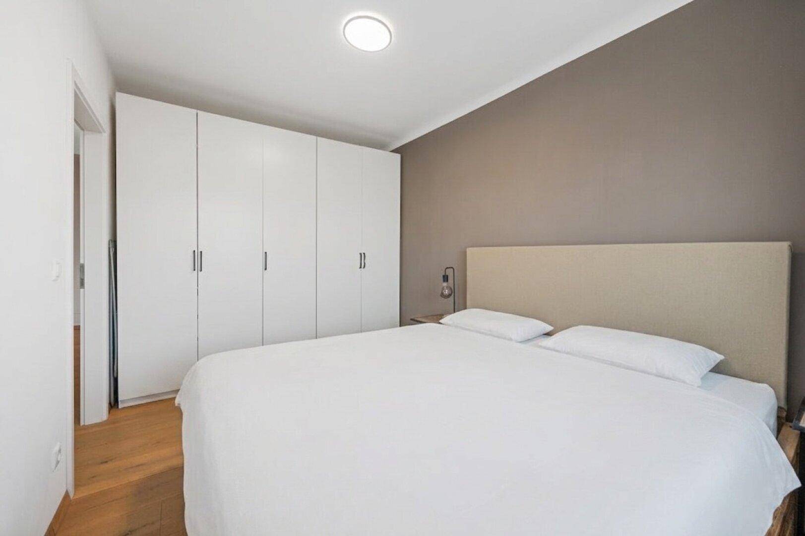 Helles Schlafzimmer mit Doppelbett und geräumigen weißen Einbauschränken entlang der Wand.