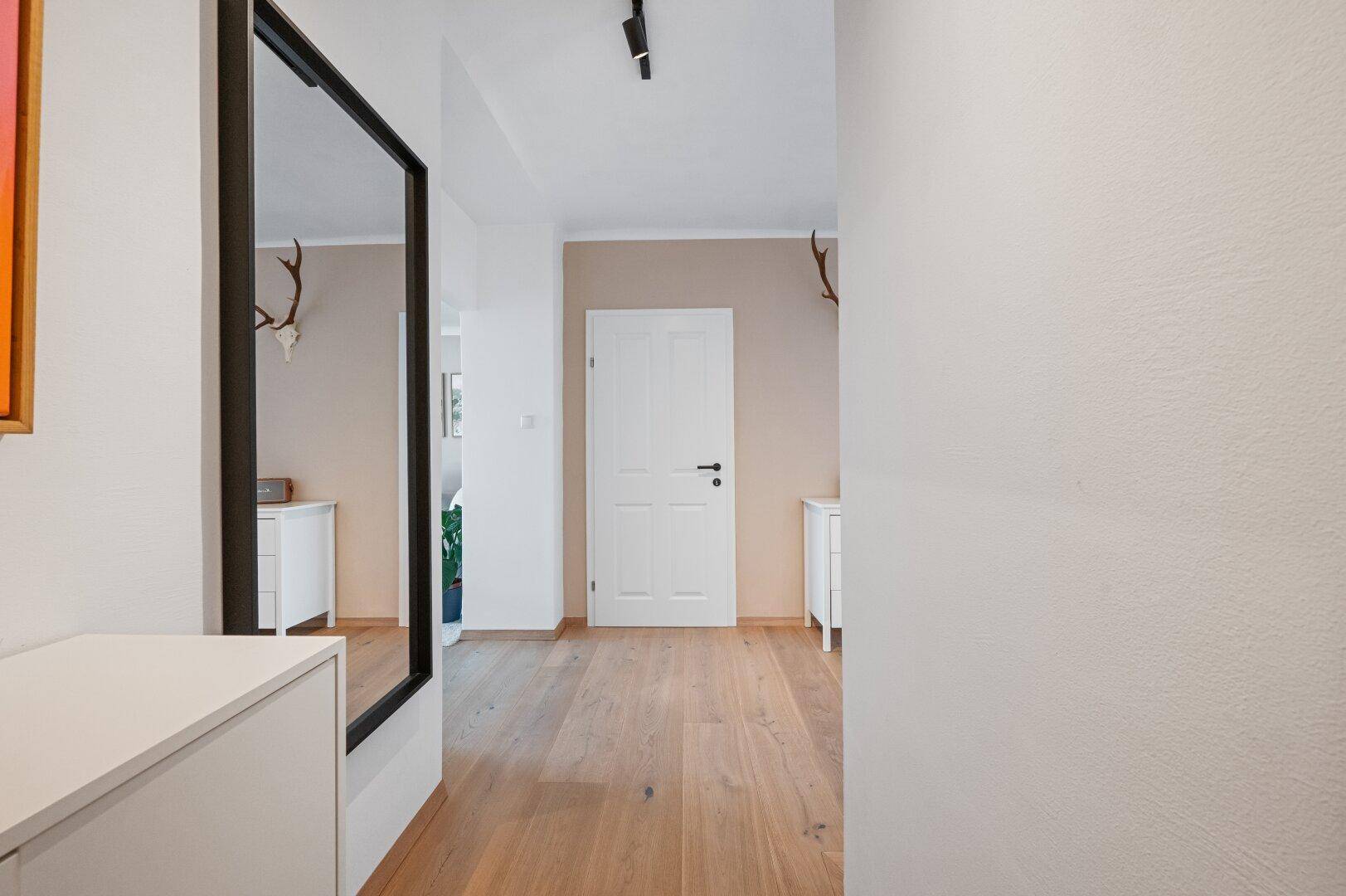 Heller Flur mit Holzboden, großem Spiegel und Hirschgeweih-Dekoration an der Wand.
