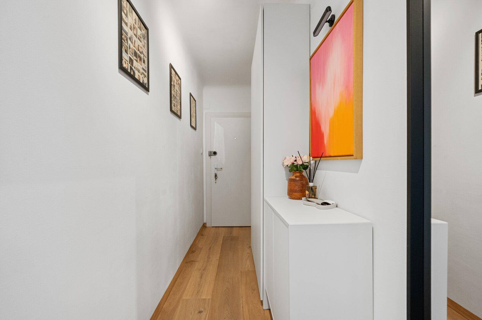 Langer, heller Flur mit Holzboden, weißer Einrichtung und moderner Wanddekoration.