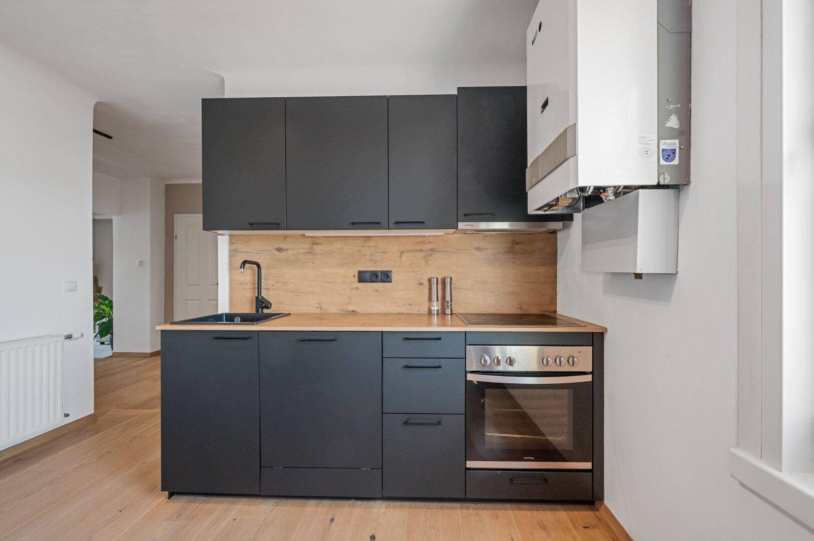 Moderne schwarze Einbauküche mit Holzrückwand, integriertem Backofen und Gastherme an der Wand.