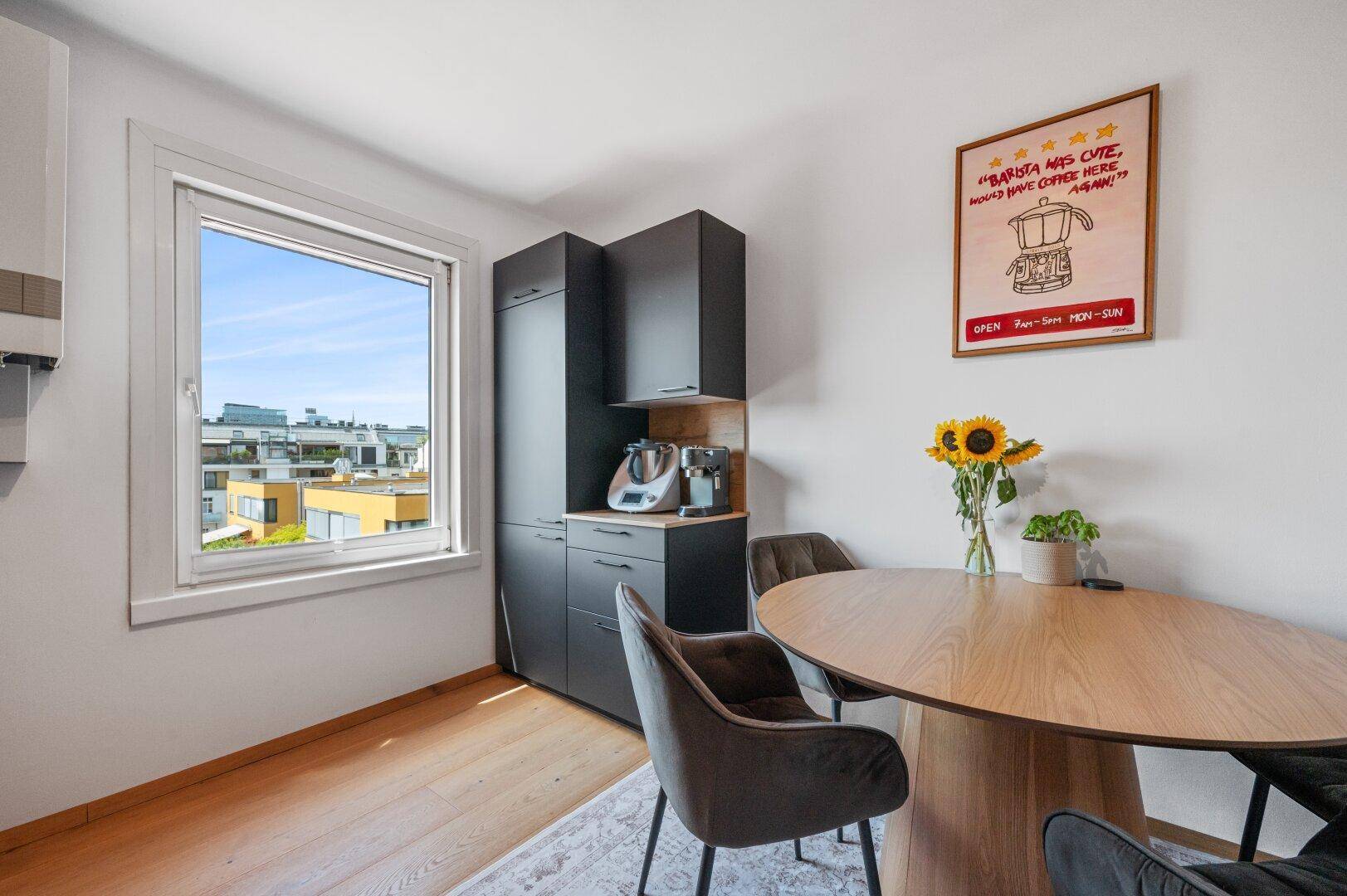 Heller Essbereich in der Küche mit Holztisch, dunklen Schränken und Fenster mit Stadtblick.