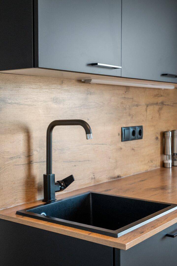 Moderne Küche mit schwarzem Spülbecken, schwarzem Wasserhahn und Holz-Arbeitsplatte.
