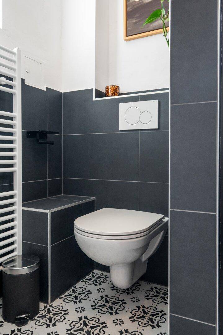 Modernes Wand-WC mit dunklen Fliesen und beheiztem Handtuchhalter im Badezimmer.