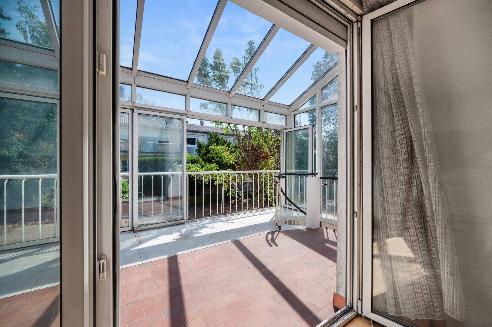 Heller Wintergarten mit Blick in den Garten und viel Tageslicht durch die Glasfront.