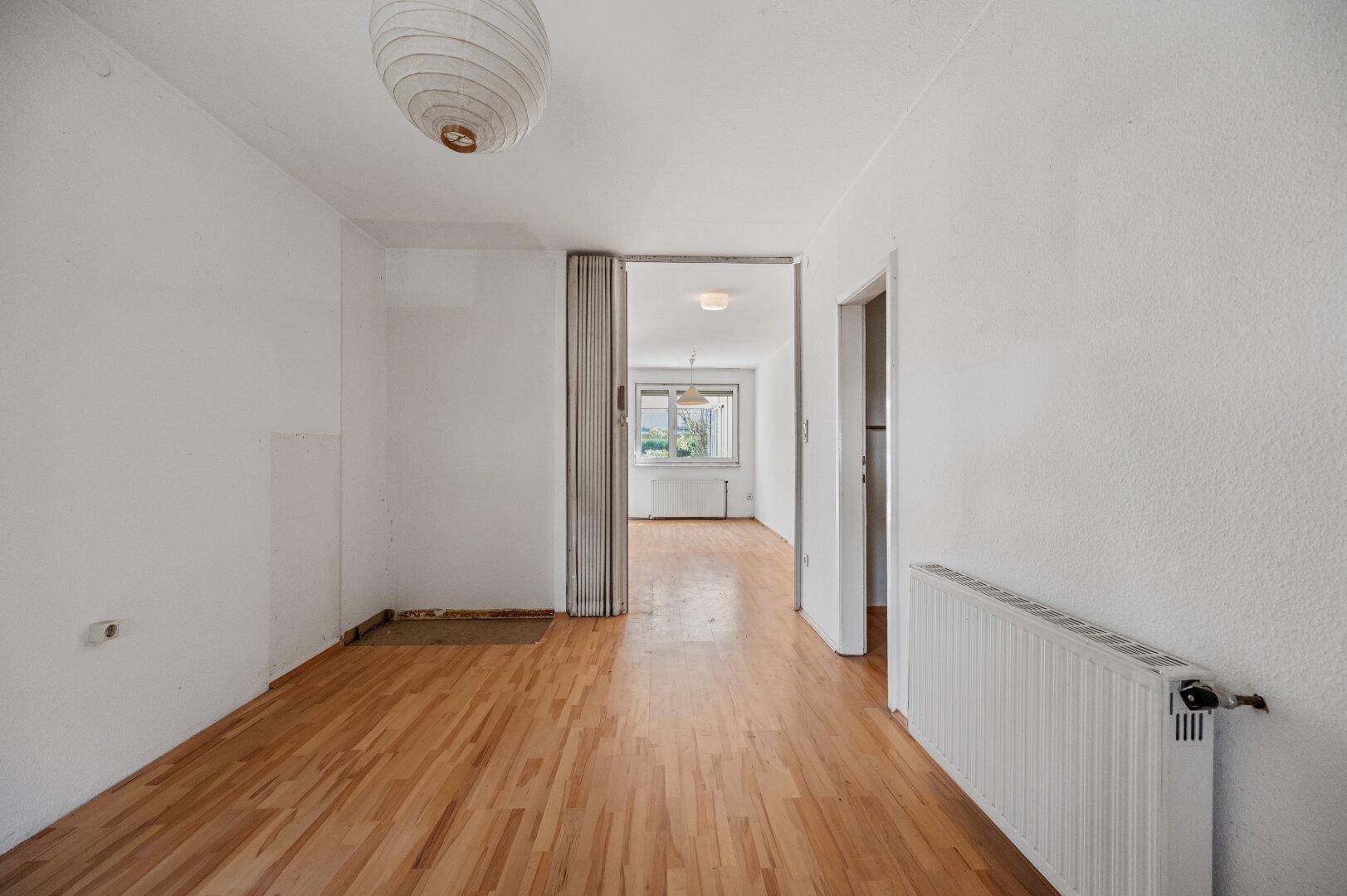 Heller Flur mit Holzboden und Zugang zu weiteren Räumen im ursprünglichen Zustand.