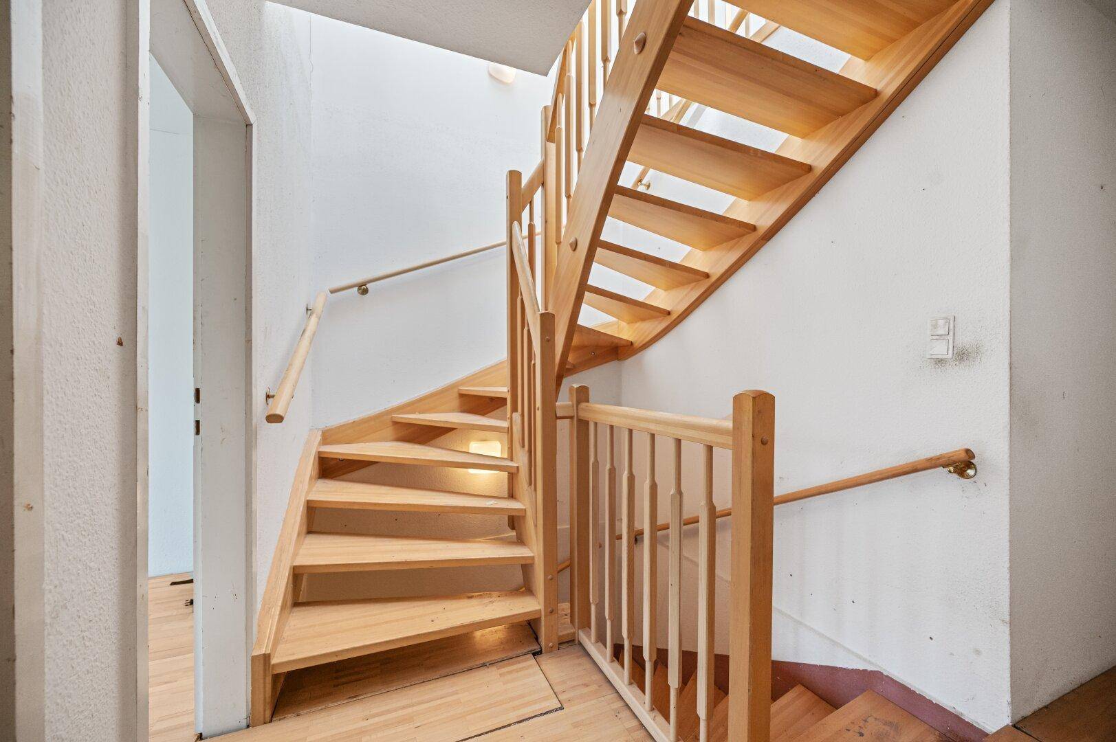 Helles Treppenhaus mit Holzstufen und Geländer, bereit für eine Modernisierung.