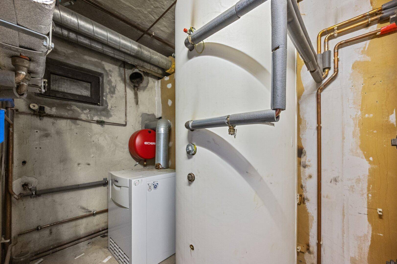 Hauswirtschaftsraum im Keller mit Warmwasserbereiter und sichtbaren Rohrleitungen.