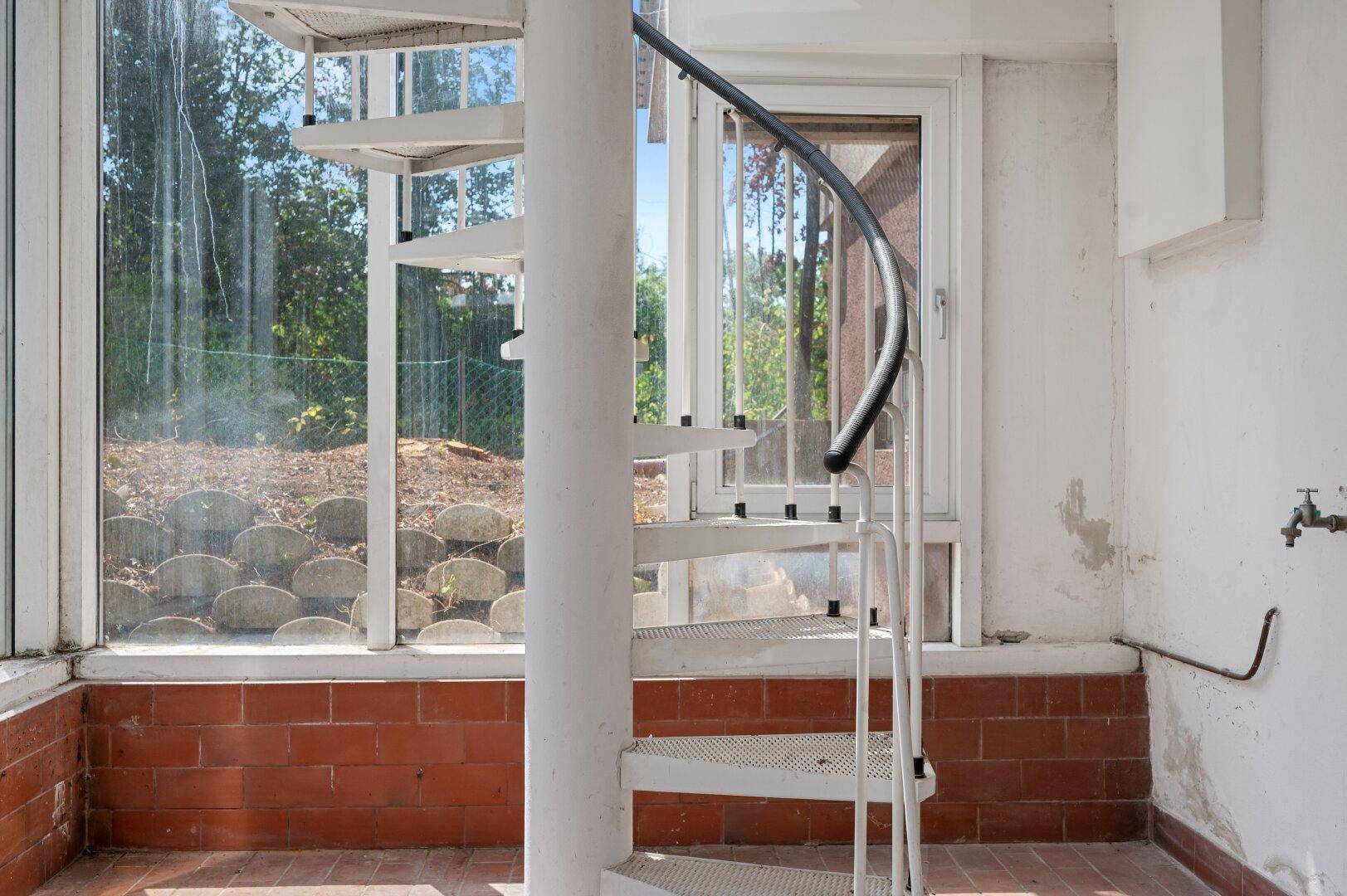 Wendeltreppe im Wintergarten mit Blick auf die umliegende Natur durch die Fenster.
