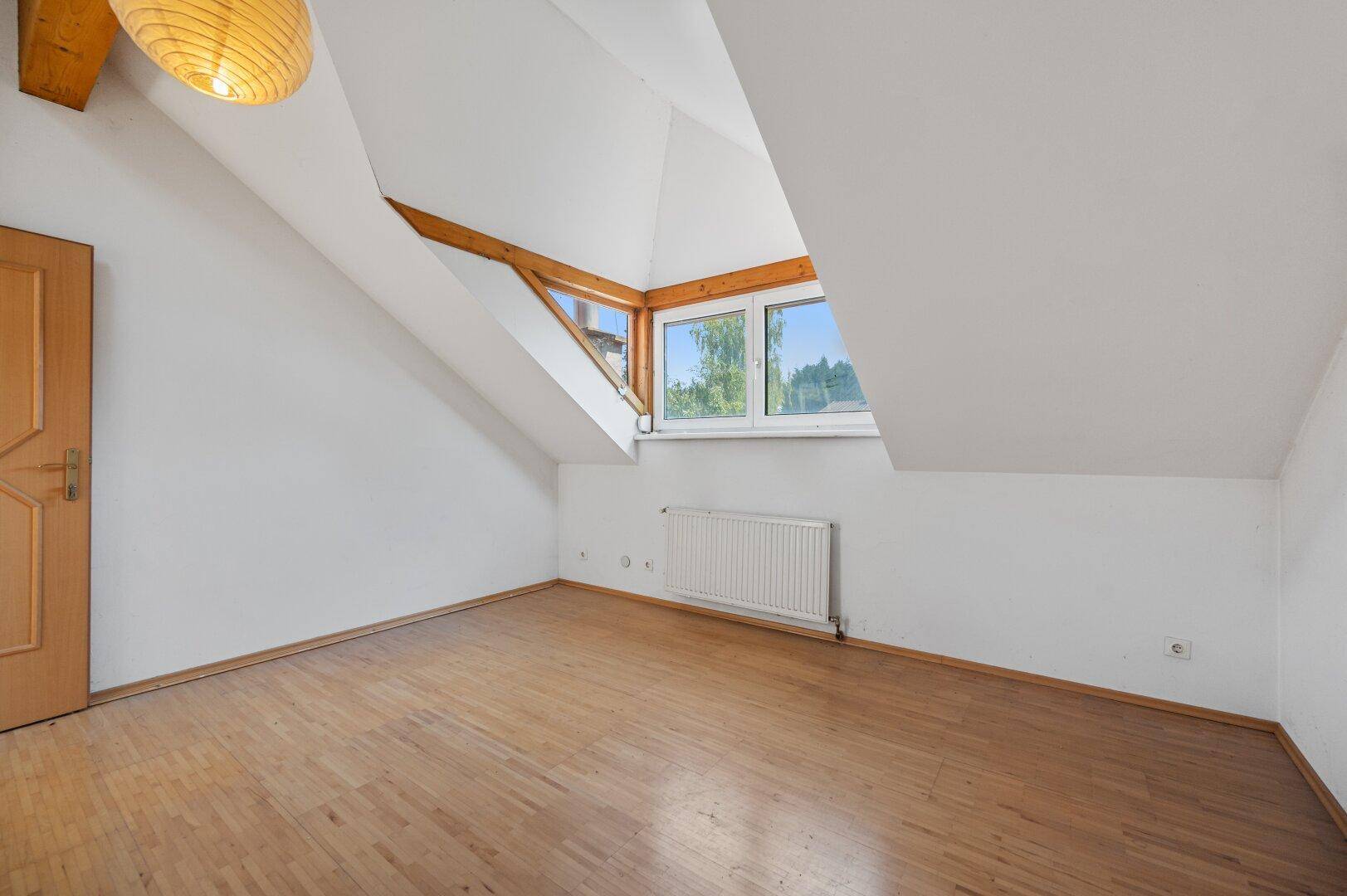 Geräumiger leerer Raum mit Dachschräge, Holzbalken und Fenster für natürliche Belichtung.