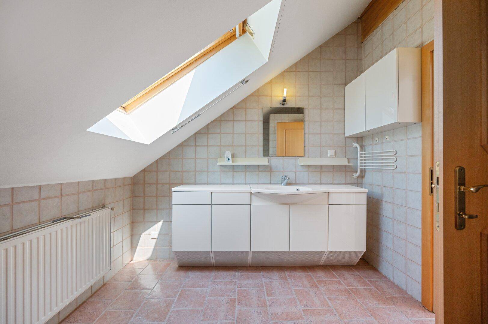 Badezimmer mit Waschbecken, Dachfenster und einfachen Fliesen, das viel Licht erhält.