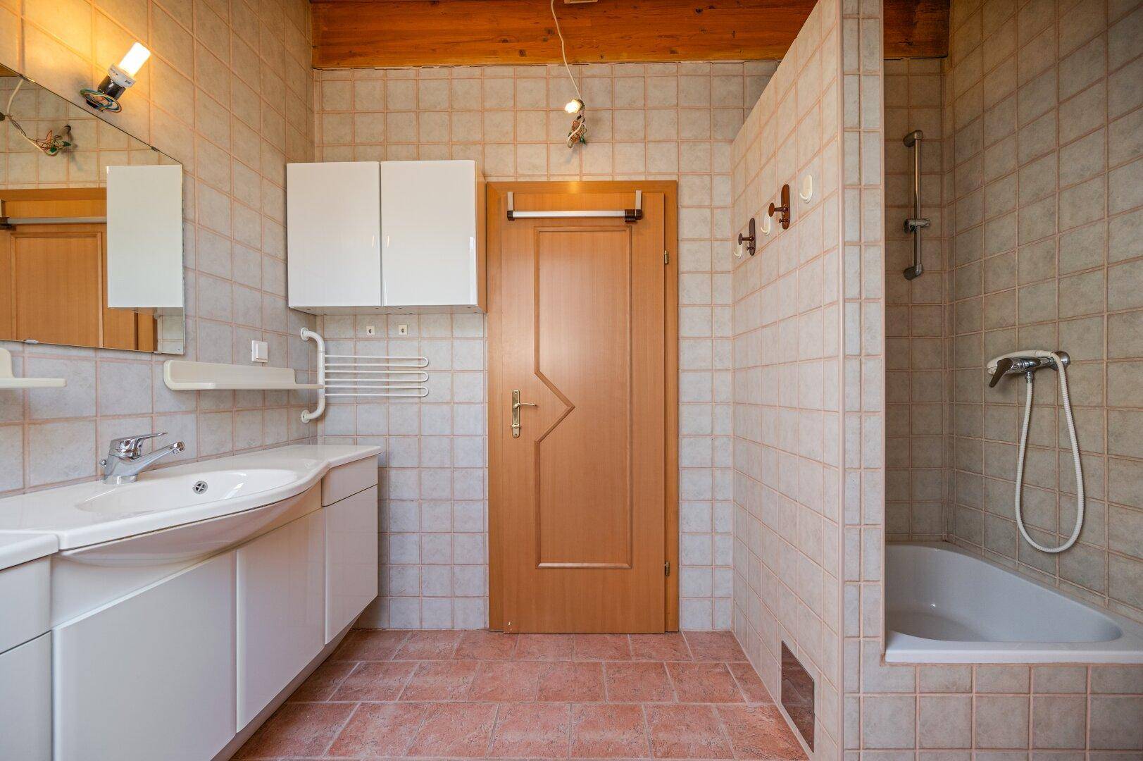 Funktionales Badezimmer mit Waschbecken, Badewanne mit Duschfunktion und einfachen Fliesen.
