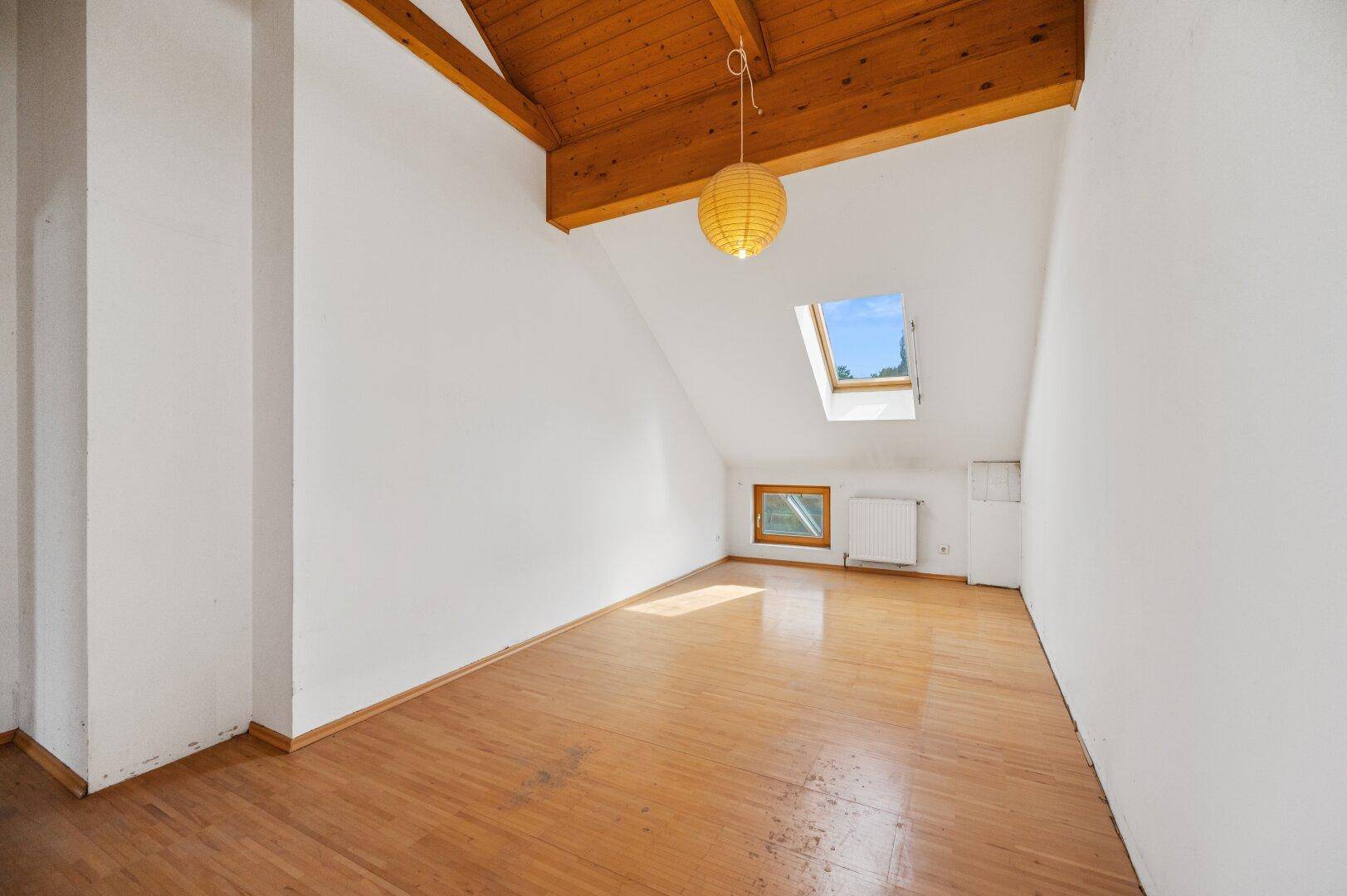 Leerer Raum mit Holzbalkendecke, Dachschräge und Oberlicht, das den Raum erhellt.