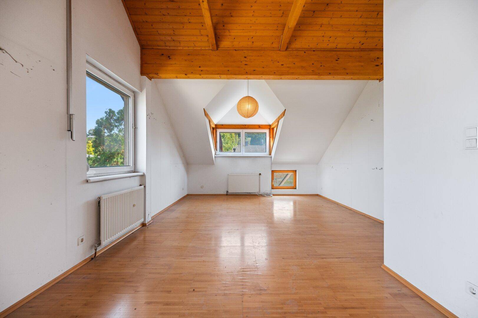 Geräumiges leeres Schlafzimmer mit Holzbalkendecke, Dachschräge und großen Fenstern.