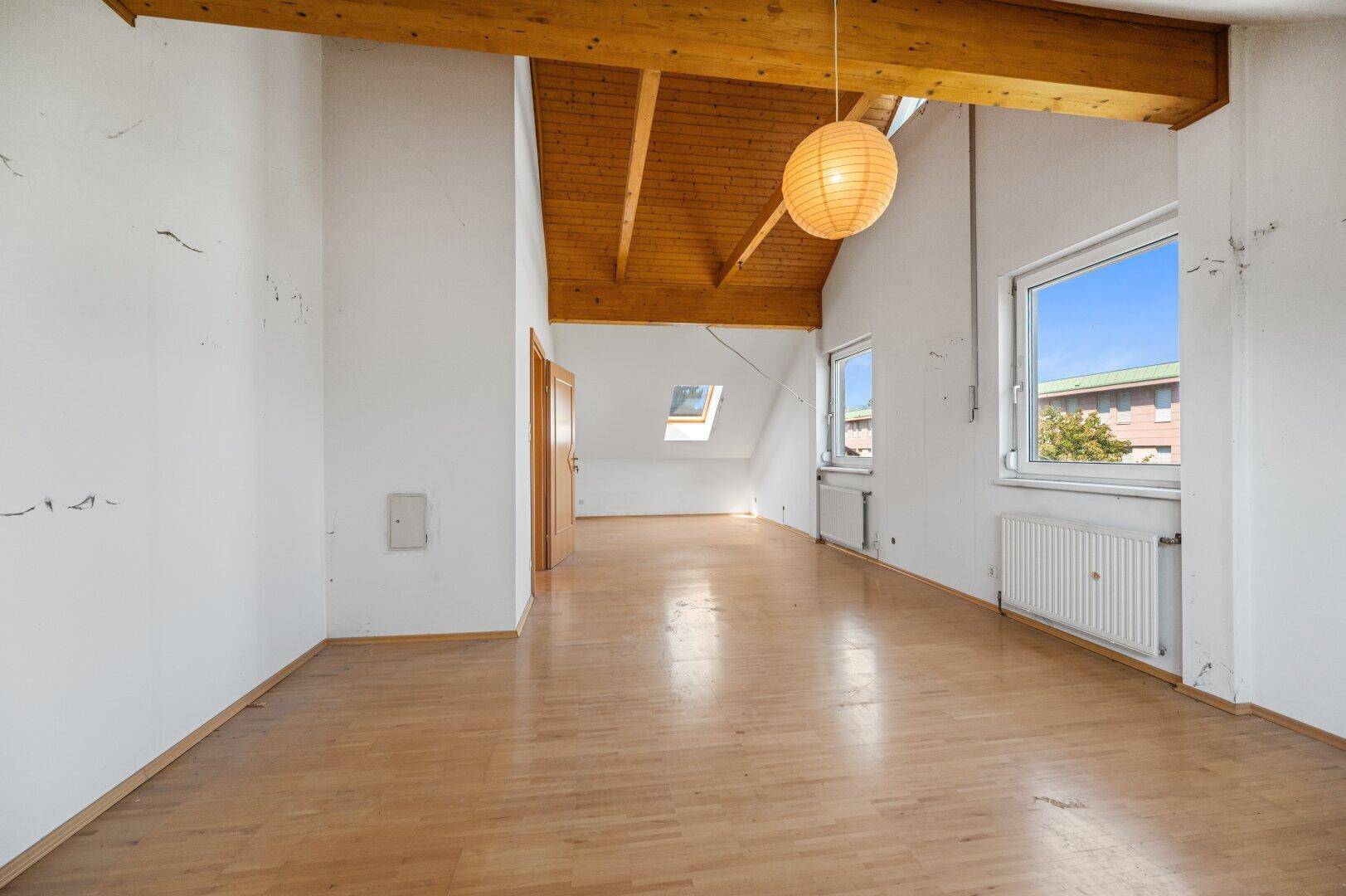 Leeres Schlafzimmer mit Holzbalkendecke, Dachschräge, großem Fenster und viel Tageslicht.