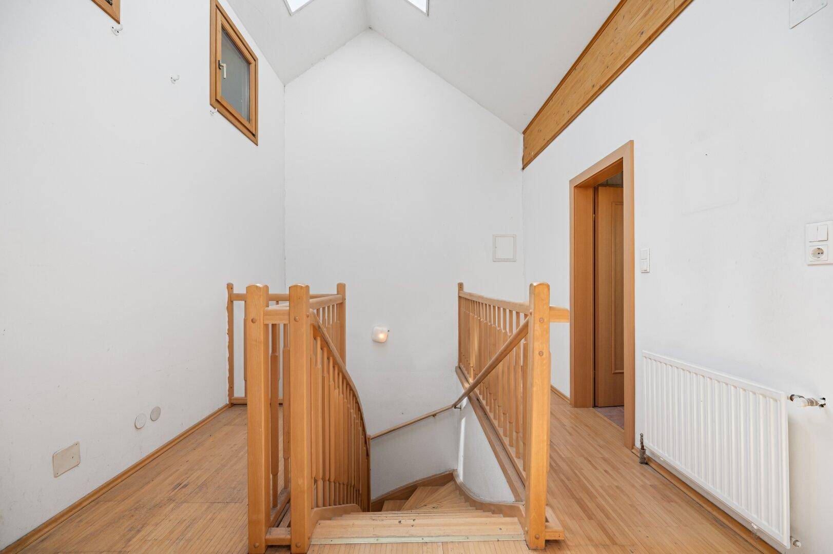Leerer Flur mit Holztreppe, Holzgeländer und Oberlichtern, die den Raum erhellen.