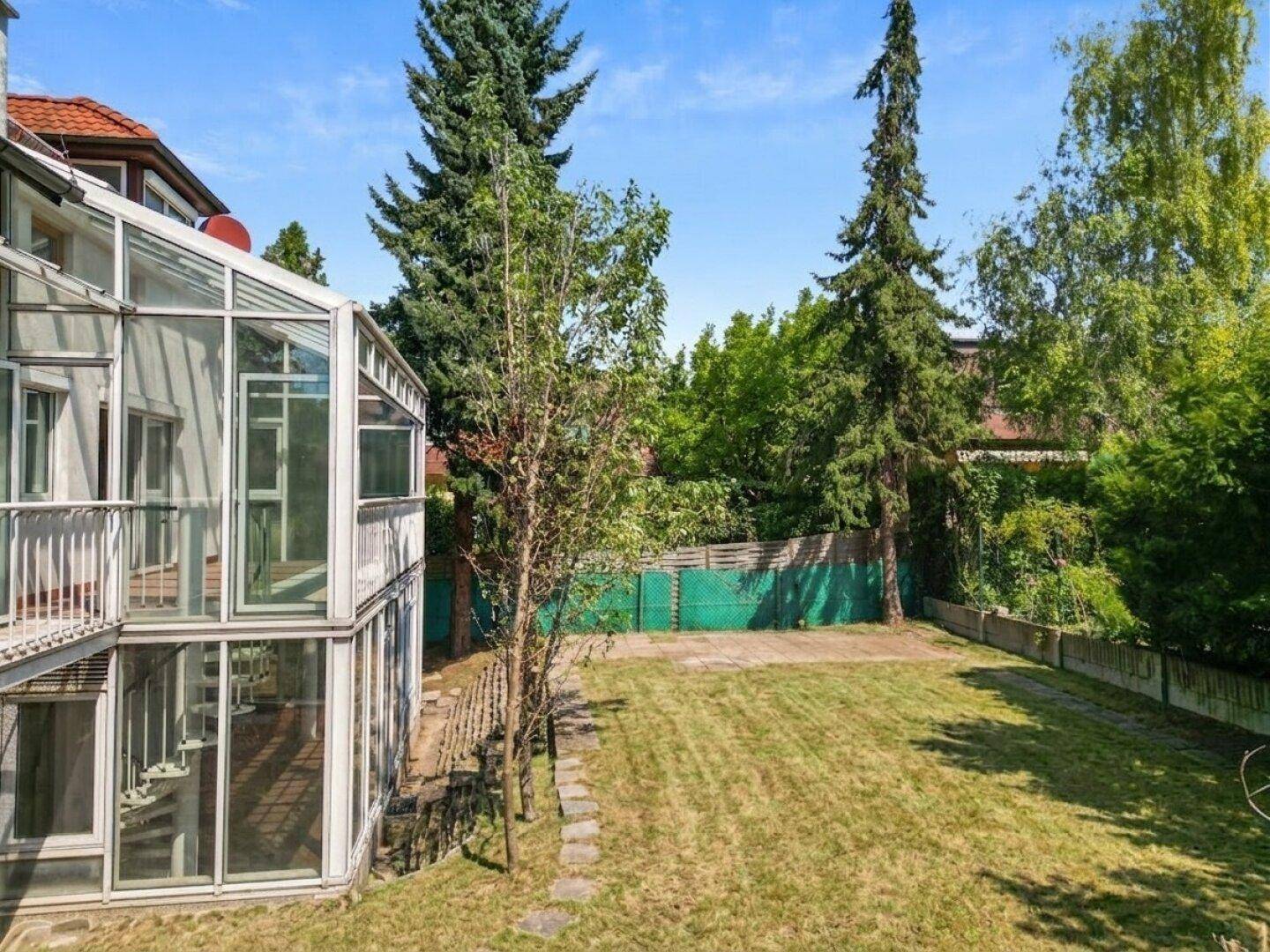 Seitenansicht des Hauses mit weitläufigem Garten und dem verglasten Anbau.
