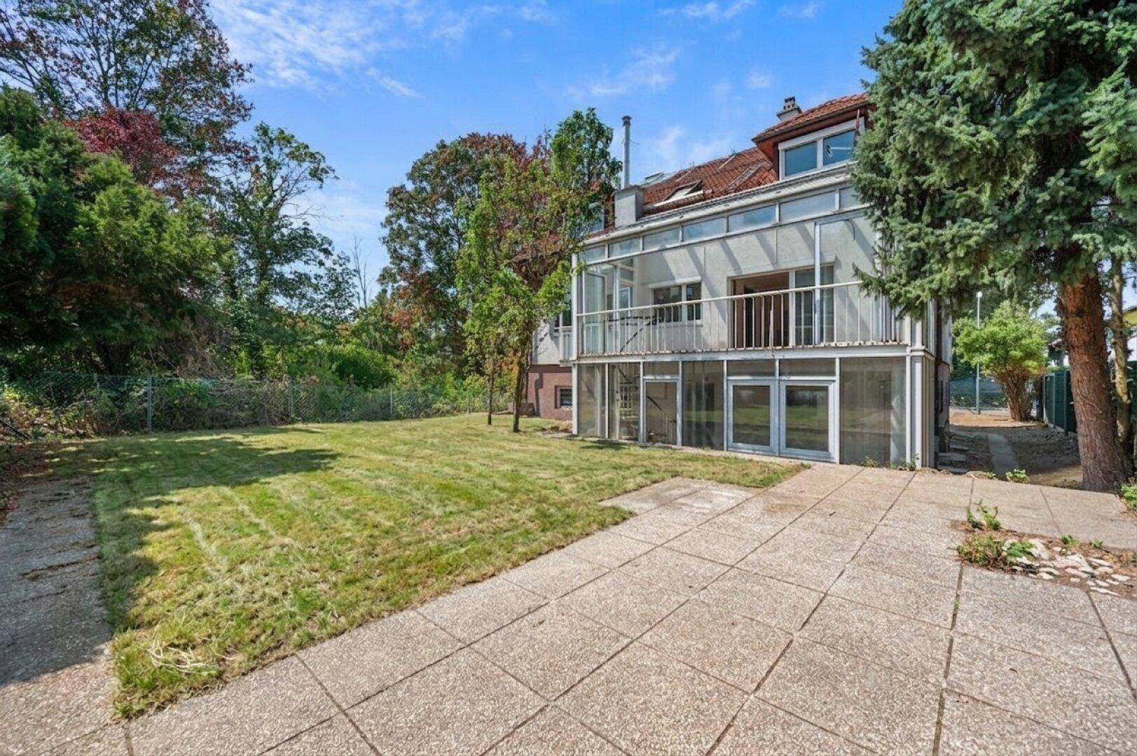 Hinteransicht des Hauses mit großem Rasenbereich und verglastem Anbau im ursprünglichen Zustand.
