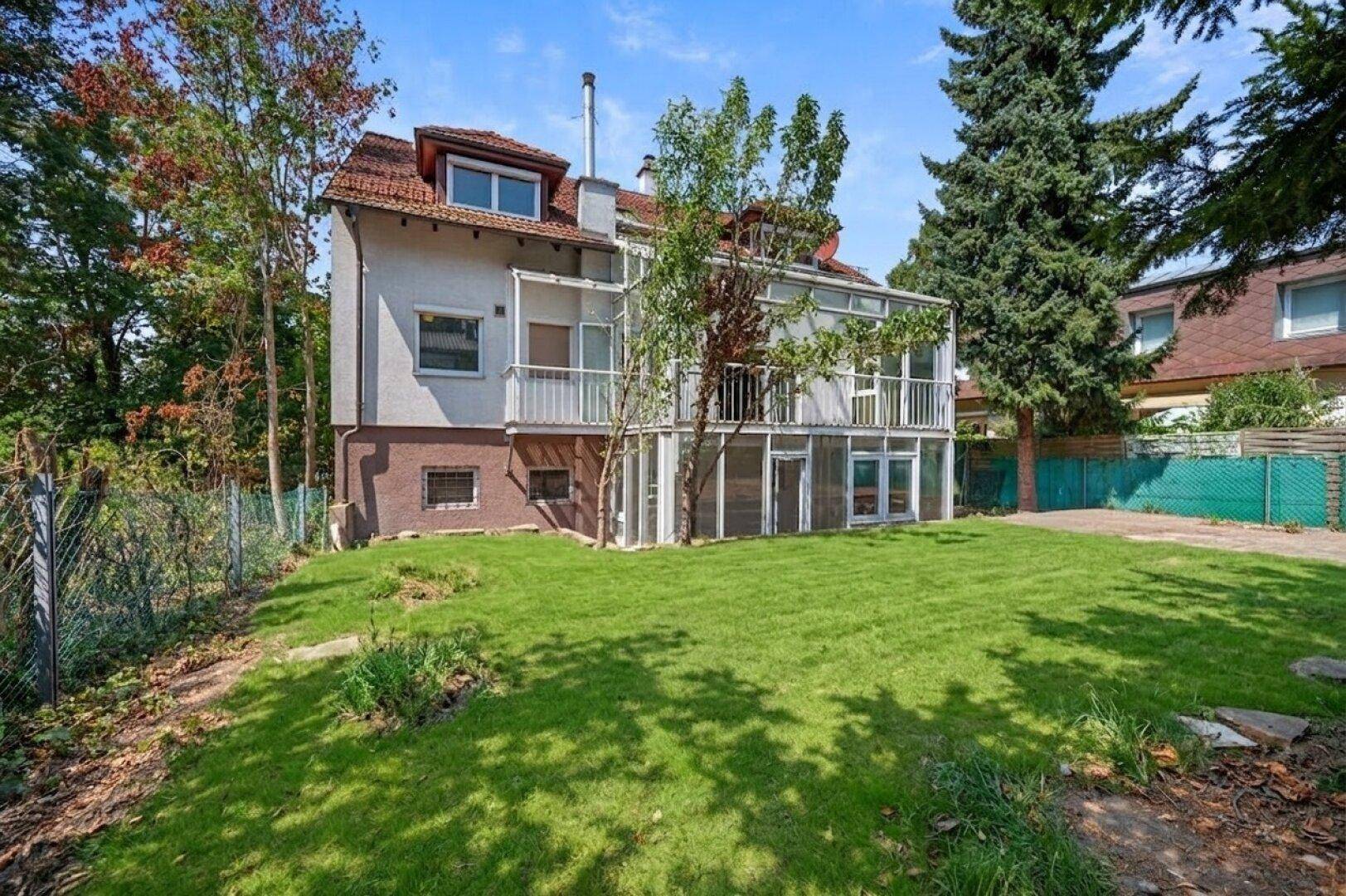 Rückansicht des Hauses mit großem Garten und dem verglasten Anbau, umgeben von Bäumen.