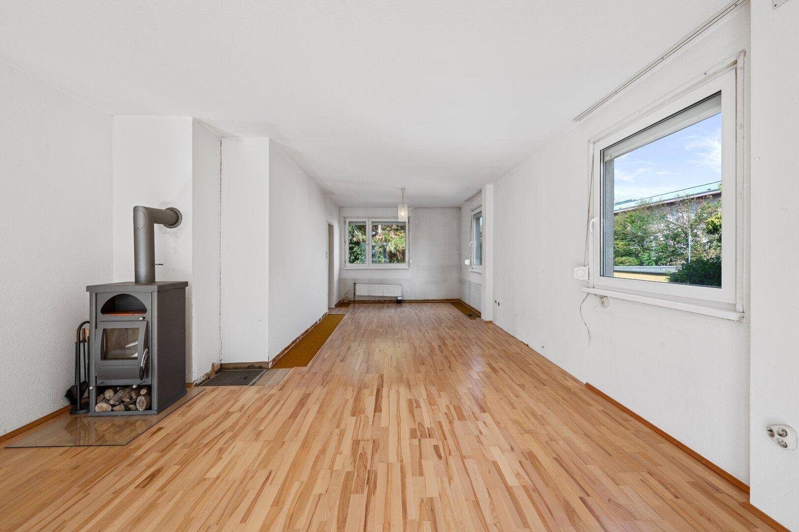 Helles Wohnzimmer mit Kaminofen und Holzboden, bereit für eine individuelle Gestaltung.