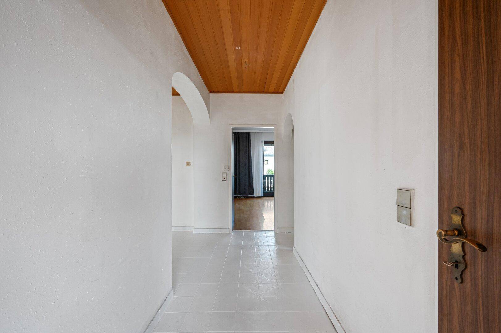 Langer Flur mit hellen Wänden, Fliesenboden und einer Holzdecke, die Gemütlichkeit ausstrahlt.