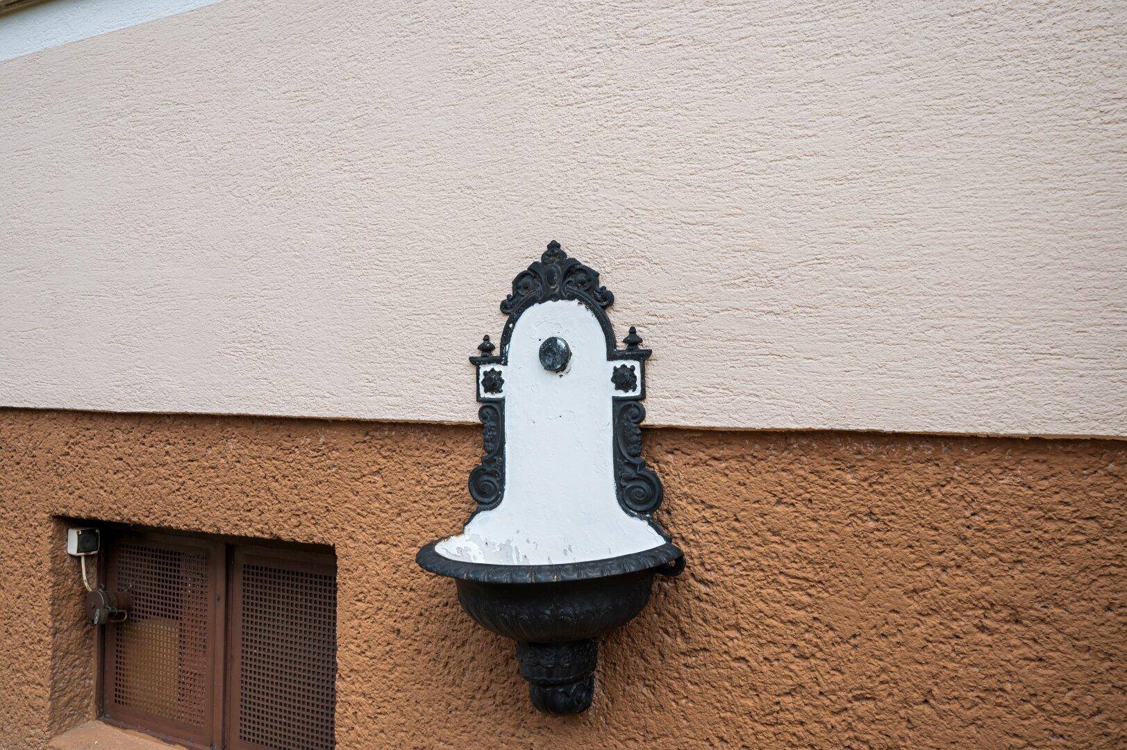 Dekorativer Wandbrunnen im klassischen Stil an der hellen Hausfassade.
