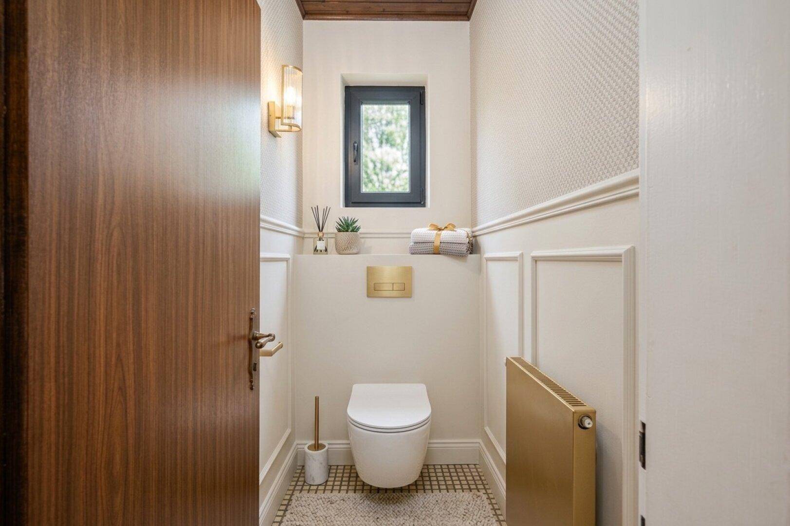 Modernes Gäste-WC mit stilvoller Wandverkleidung, goldenen Akzenten und einem Fenster.