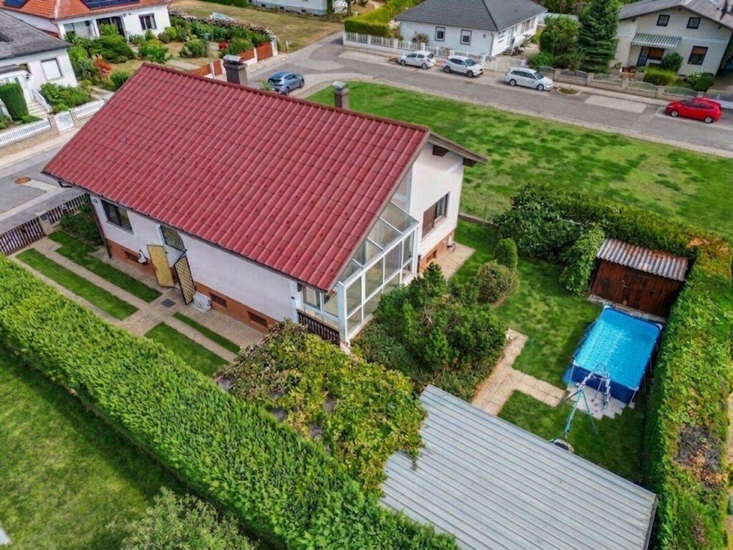 Rückansicht des Hauses mit kleinem Pool, Gartenhaus und verglastem Wintergarten im Grünen.