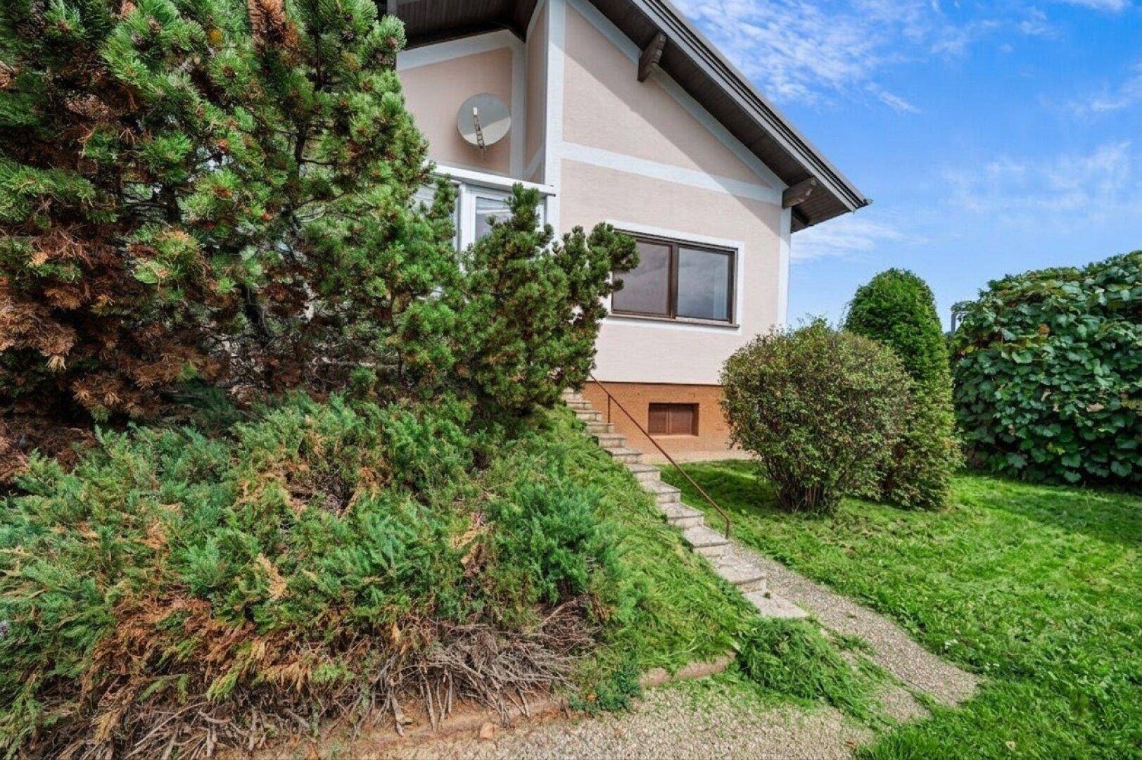 Seitenansicht des Hauses mit üppiger Bepflanzung und einer Außentreppe.