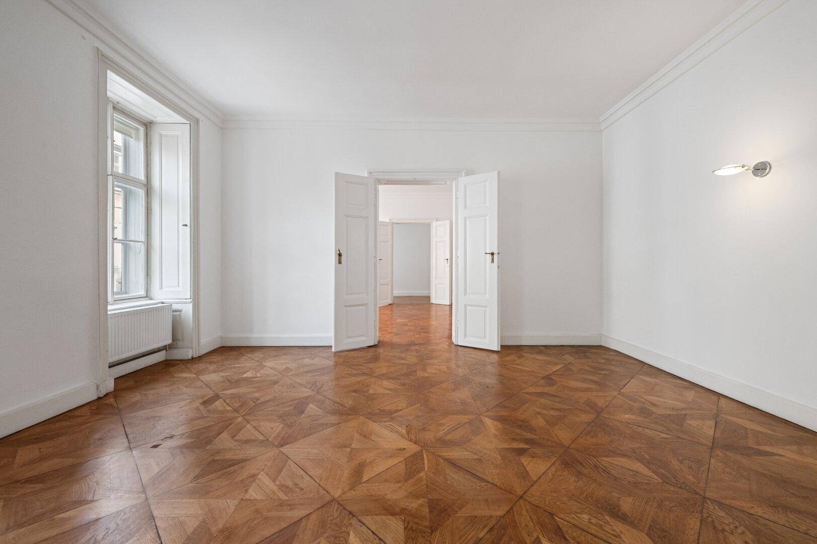 Heller, leerer Raum mit Fischgrätparkett, hohen Decken und einem großen Fenster.
