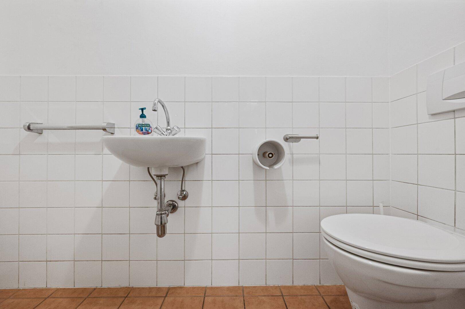 Einfache Gästetoilette mit Waschbecken, WC und weißen Wandfliesen.