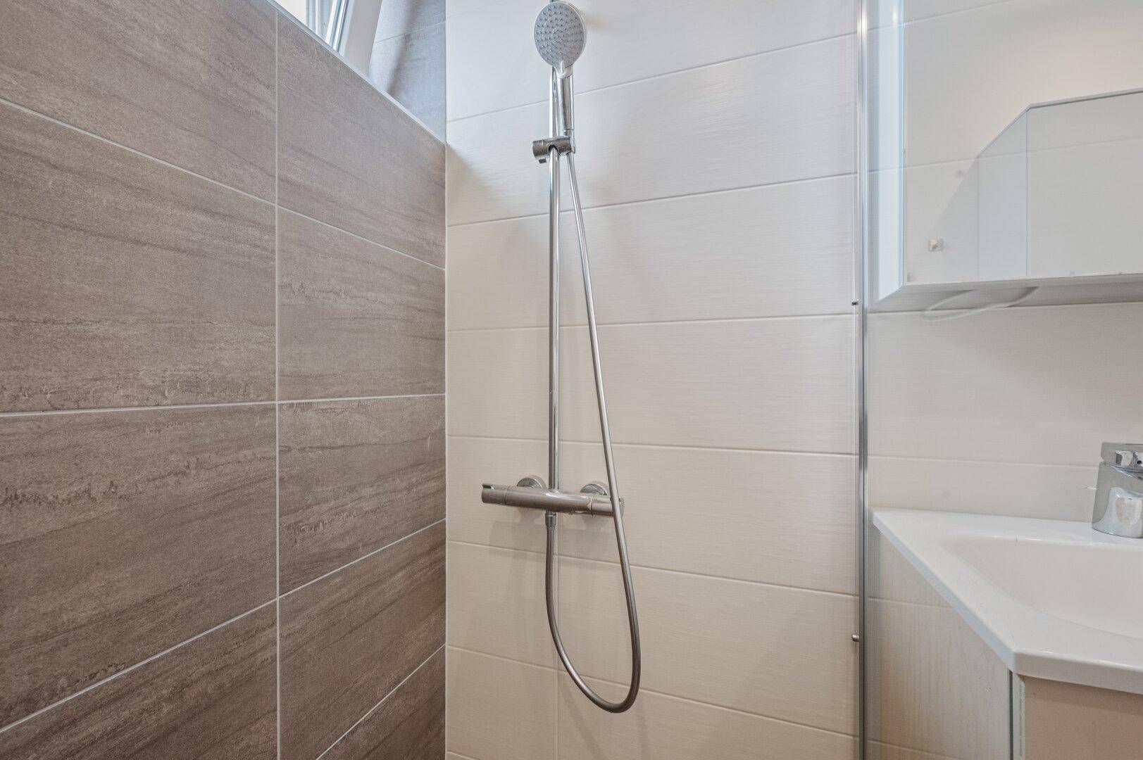 Detailansicht der modernen begehbaren Dusche mit Handbrause und eleganten Fliesen.