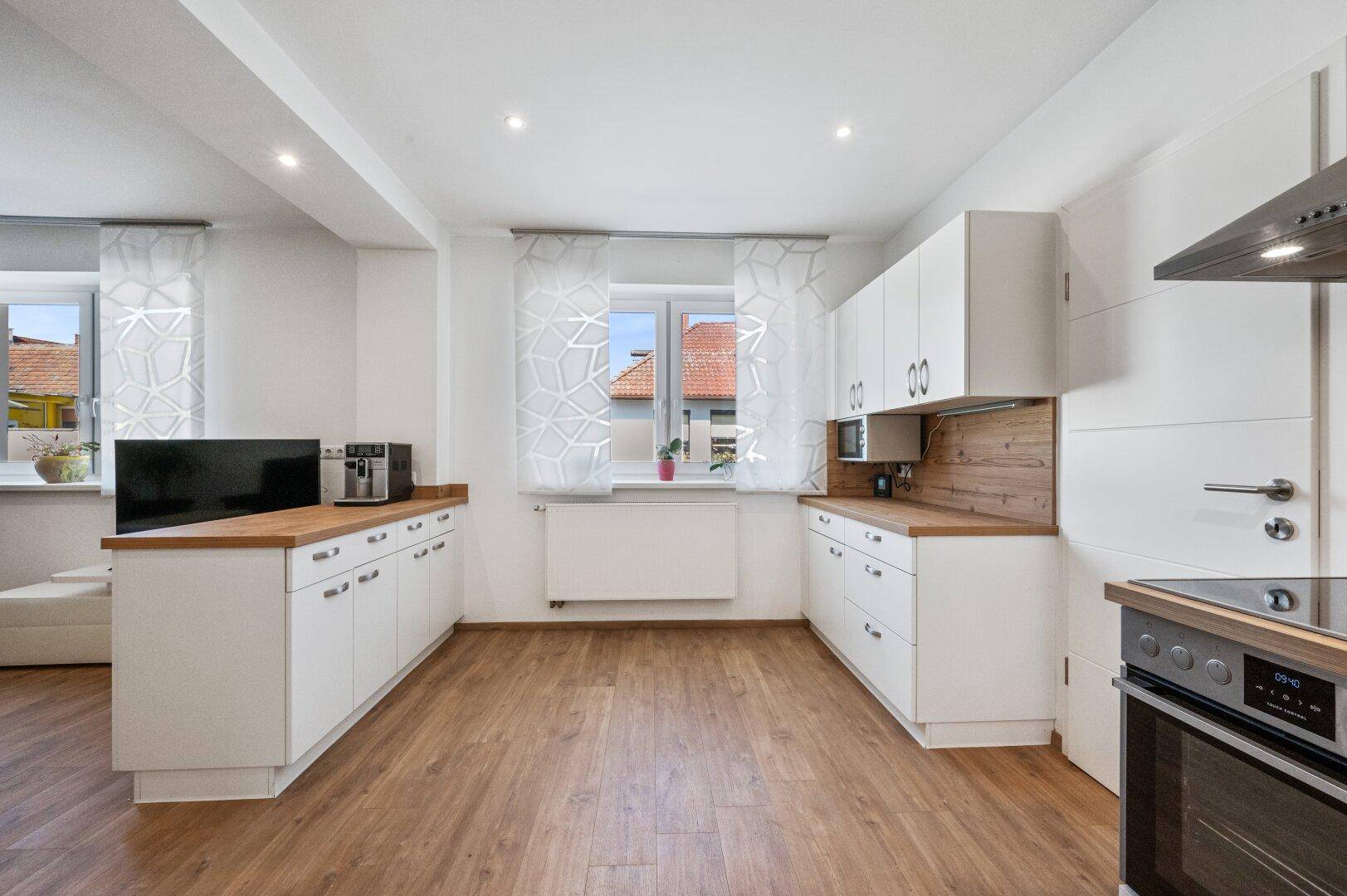 Moderne Einbauküche mit weißen Schränken, Holz-Arbeitsplatten und integrierten Geräten.