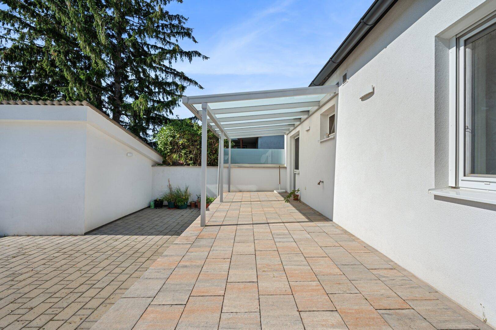 Lange, überdachte Terrasse mit gepflastertem Boden, die zum Entspannen im Freien einlädt.