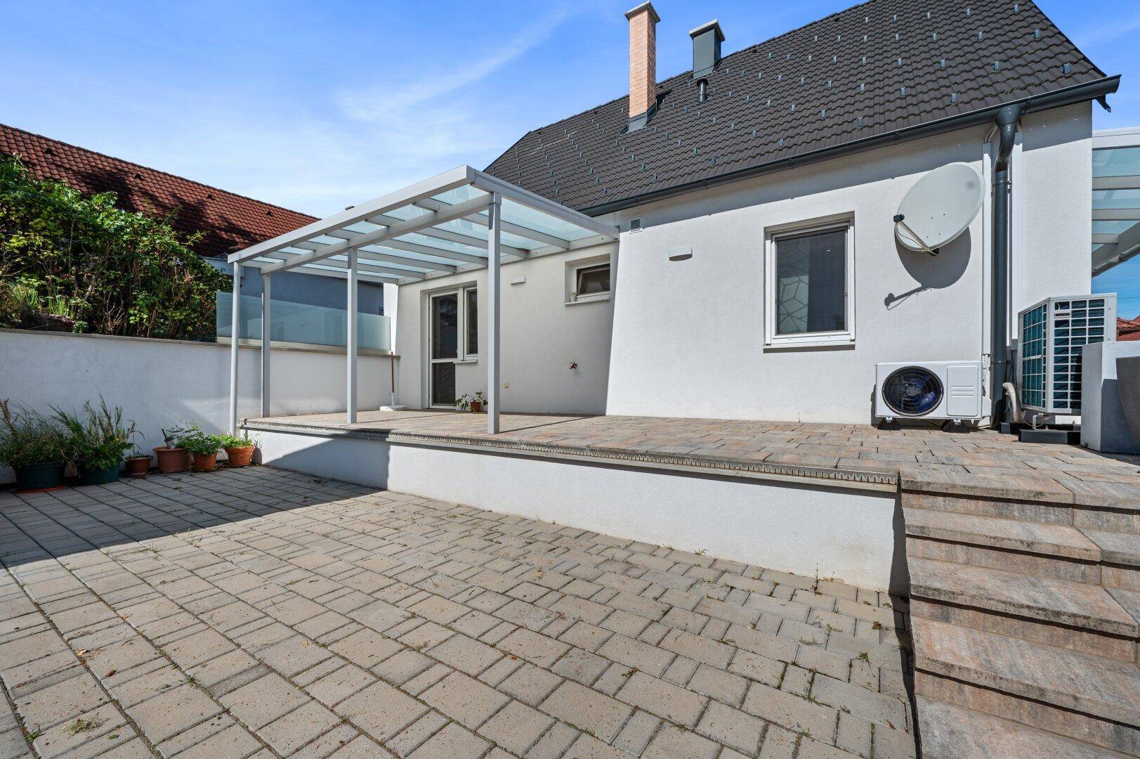 Überdachte Terrasse am Haus mit gepflastertem Bereich und Außeneinheit der Klimaanlage.
