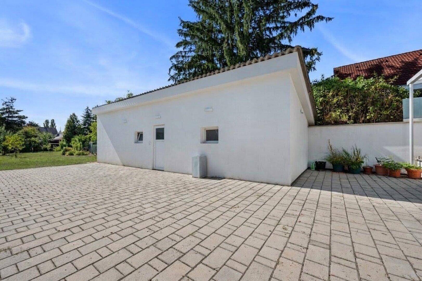 Freistehende Garage mit gepflasterter Zufahrt und angrenzendem Gartenbereich.