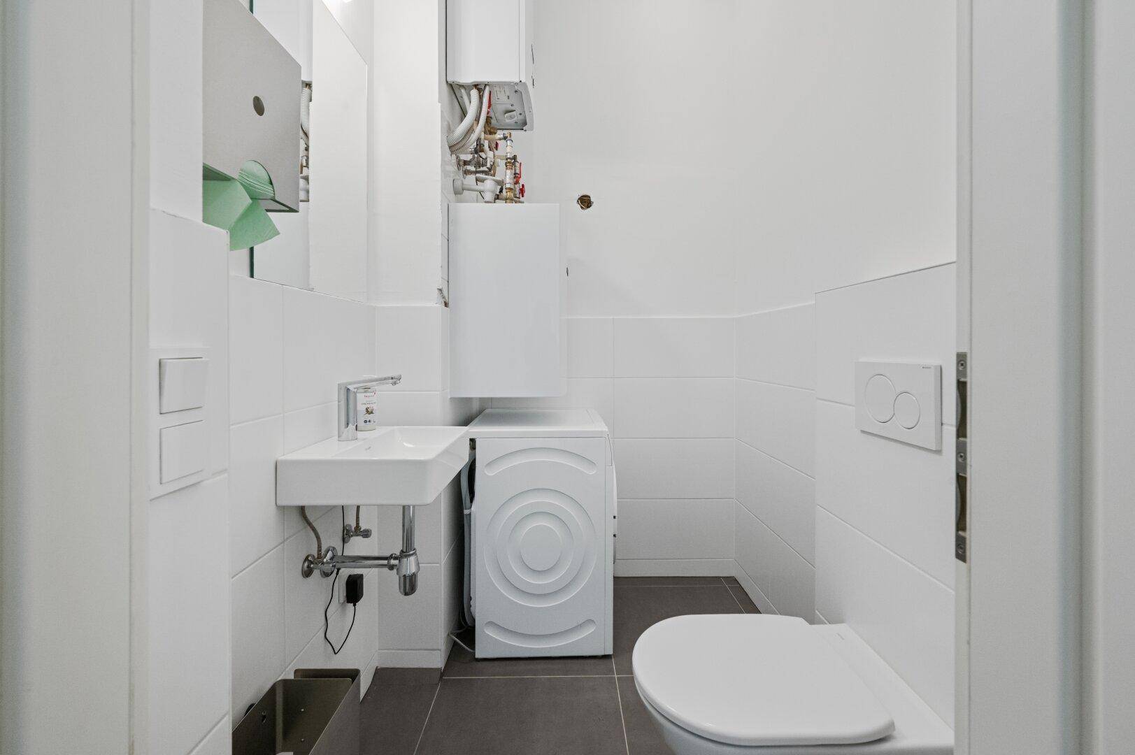 Kleines WC mit Waschbecken, Toilette und integrierter Waschmaschine, praktisch und platzsparend.