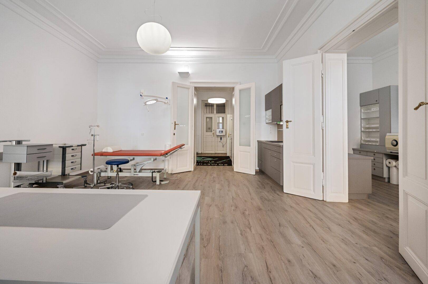 Ordinationsraum mit medizinischer Ausstattung und Blick in den Flur sowie angrenzende Funktionsräume.