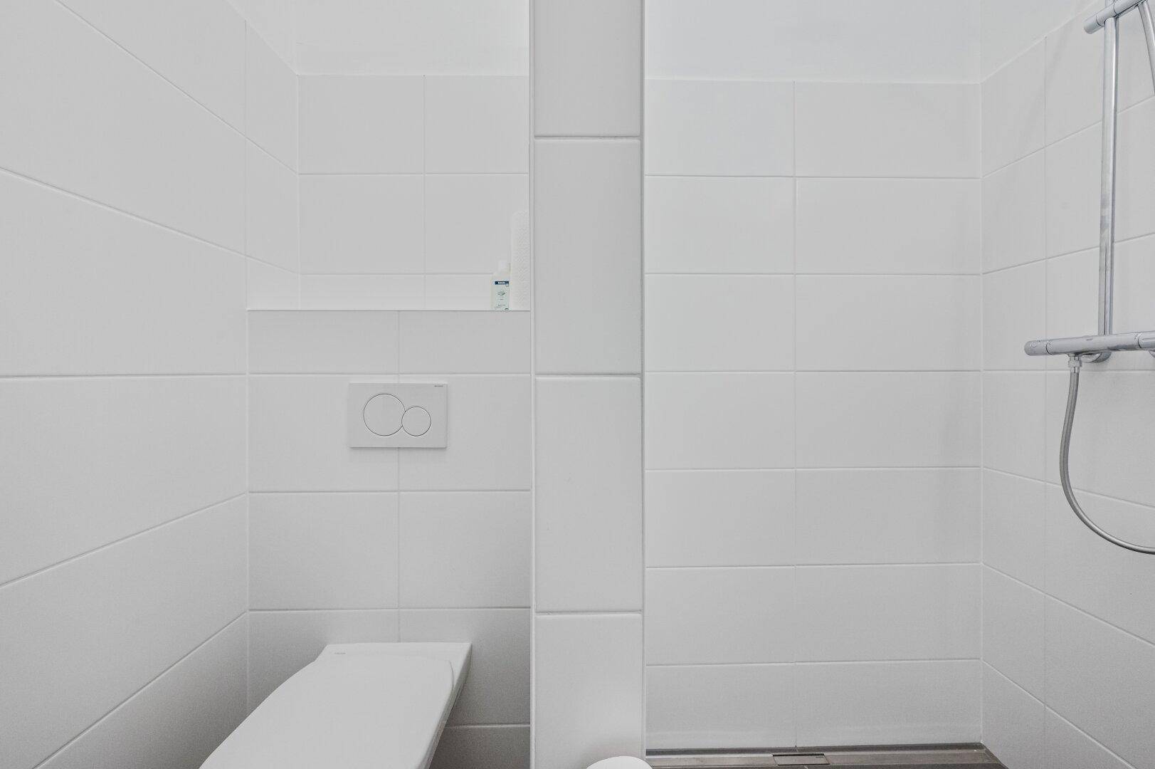 Detaillierte Ansicht des Duschbereichs mit weißen Fliesen und moderner Wandtoilette.